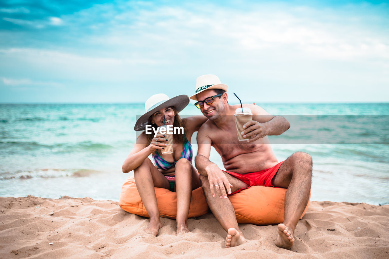 Mature couple having drinks while sitting at beach