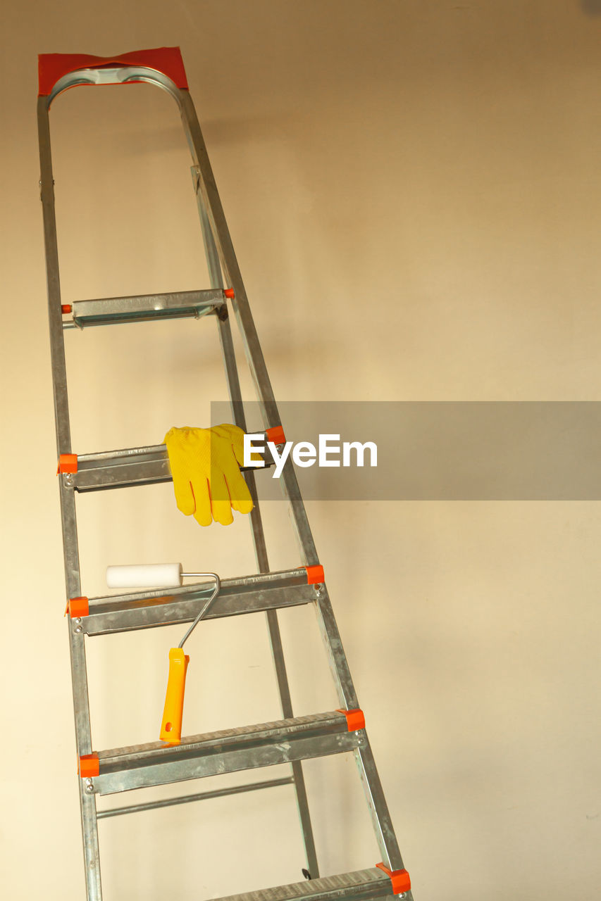 Yellow work gloves on a stepladder against the background of an empty wall. 