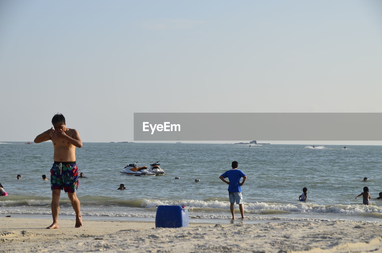 Full length of shirtless man walking at beach against clear sky