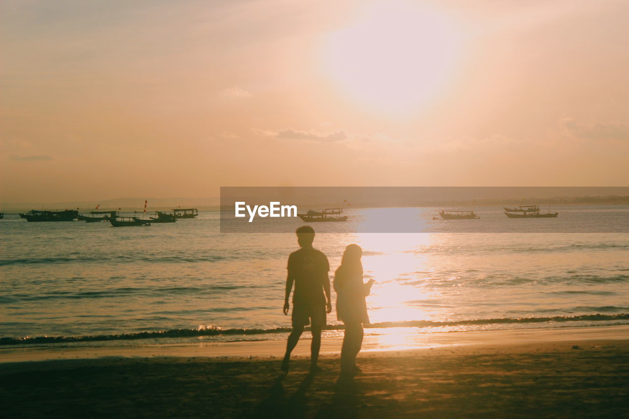 Men standing on beach against sky during sunset