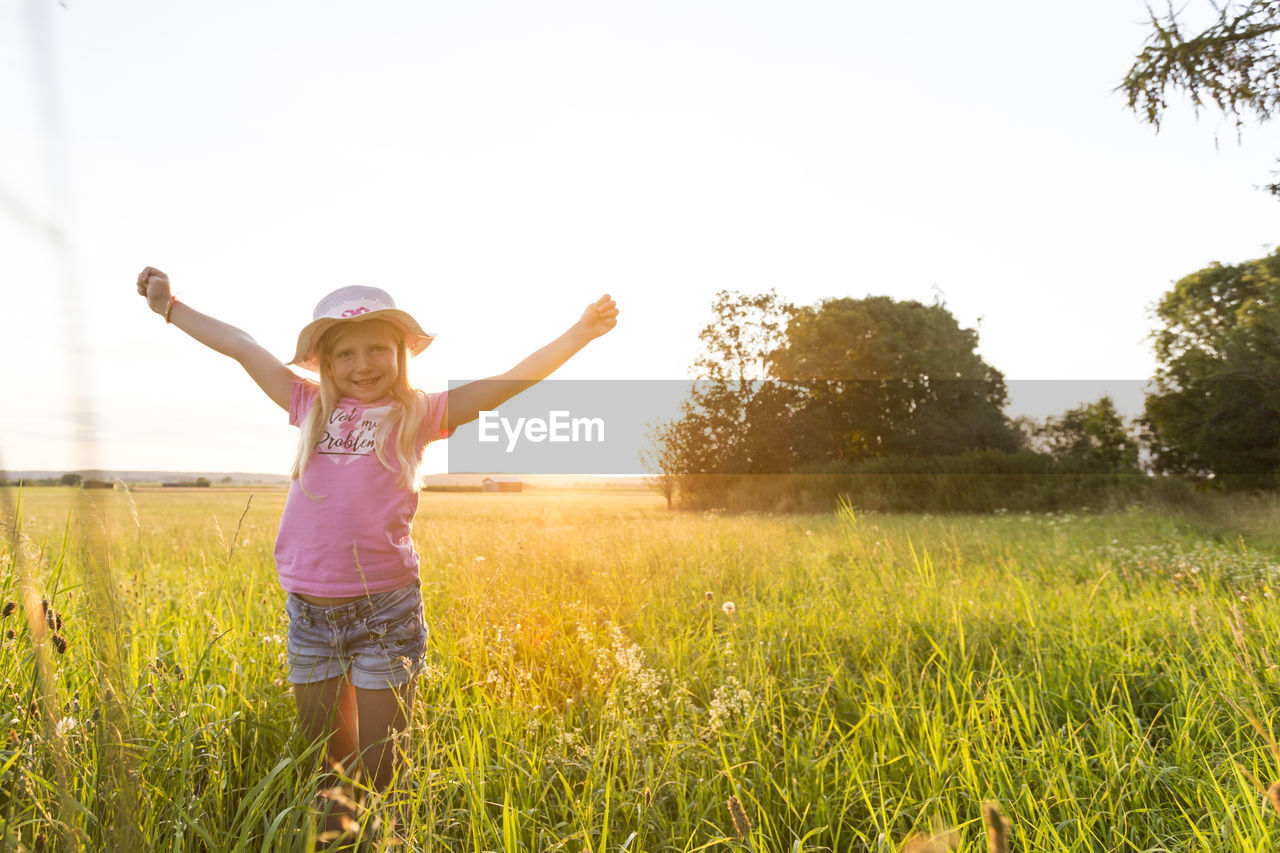 Cute girl standing amidst plants against sky during sunset