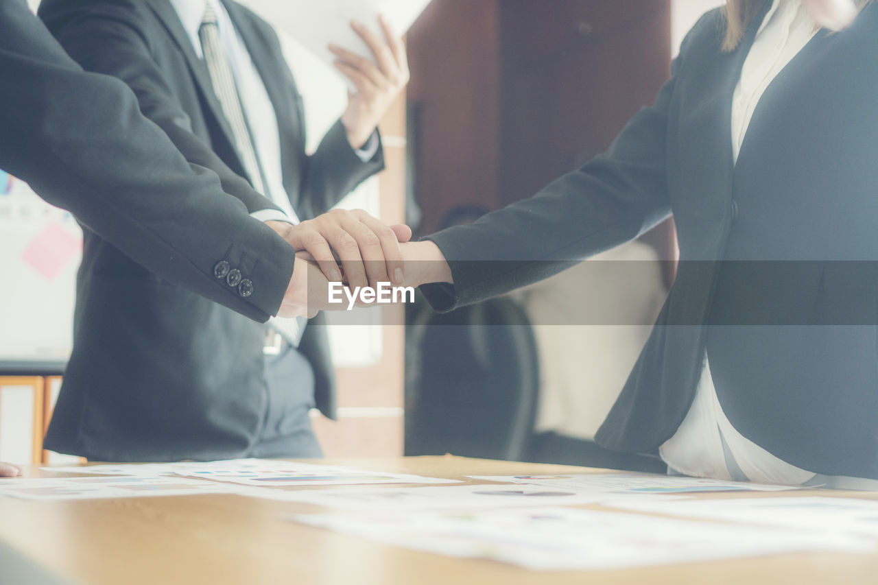 Close-up of business colleagues stacking hands while huddling in office