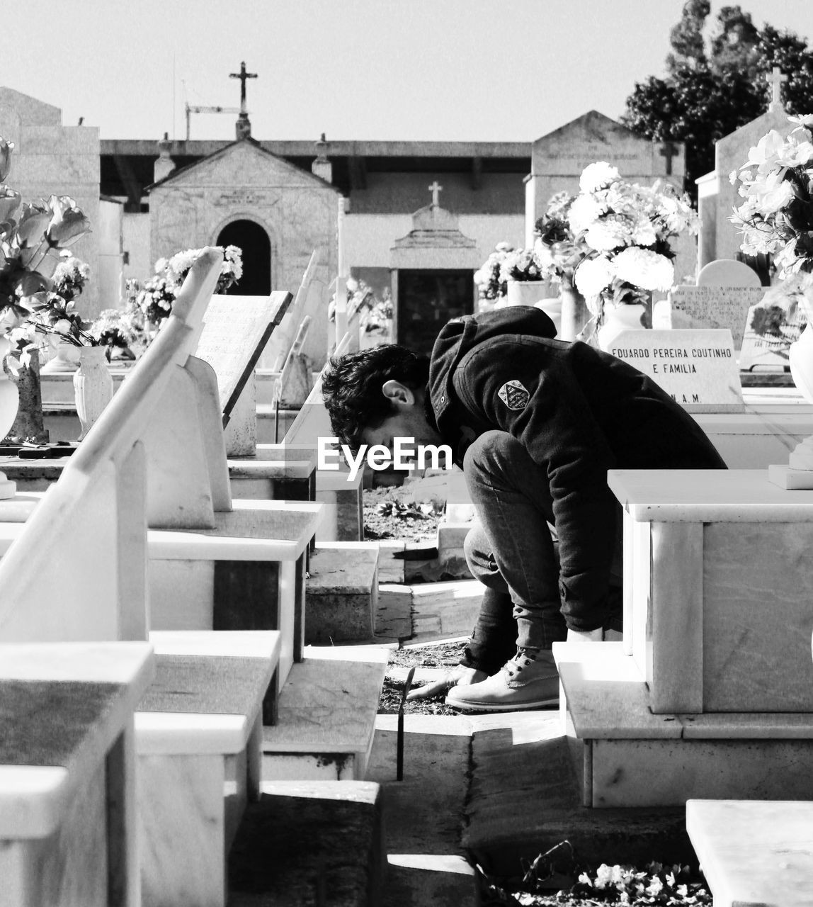 Sad young man sitting amidst tombstones in cemetery