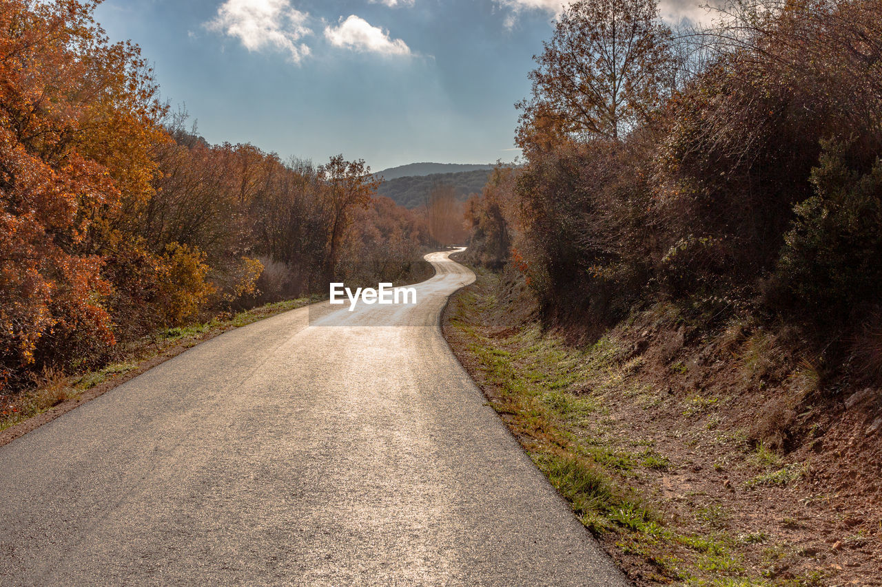 Asphalt road with curves in autumn and sky with clouds