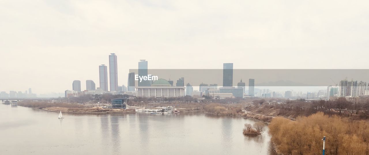 Buildings by river against sky in city