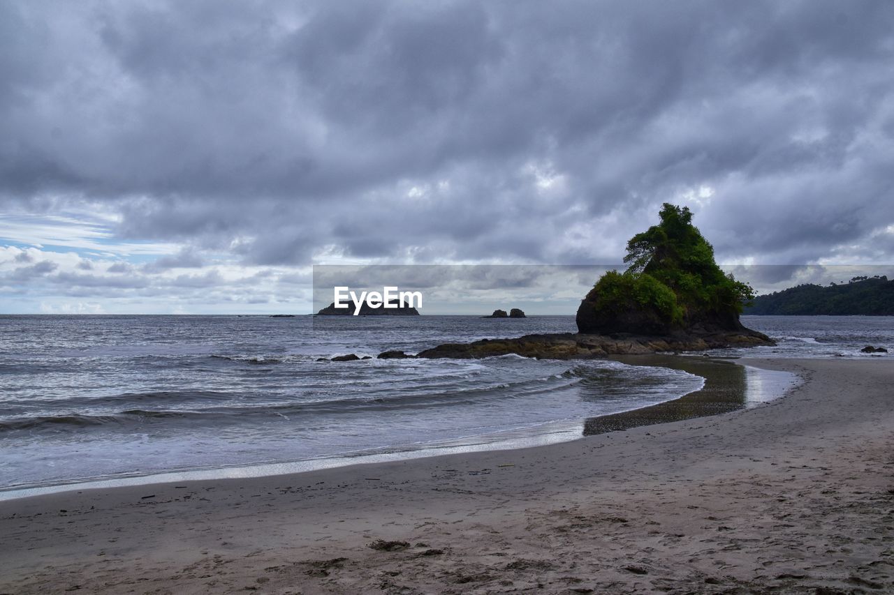 land, beach, sea, water, sky, cloud, body of water, ocean, sand, shore, wave, wind wave, coast, beauty in nature, scenics - nature, nature, environment, horizon, coastline, storm, landscape, travel destinations, overcast, dramatic sky, travel, motion, tranquility, storm cloud, no people, outdoors, rock, water's edge, holiday, tourism, seascape, trip, tranquil scene, cloudscape, island, bay, vacation, sports, non-urban scene, idyllic, day, sunset