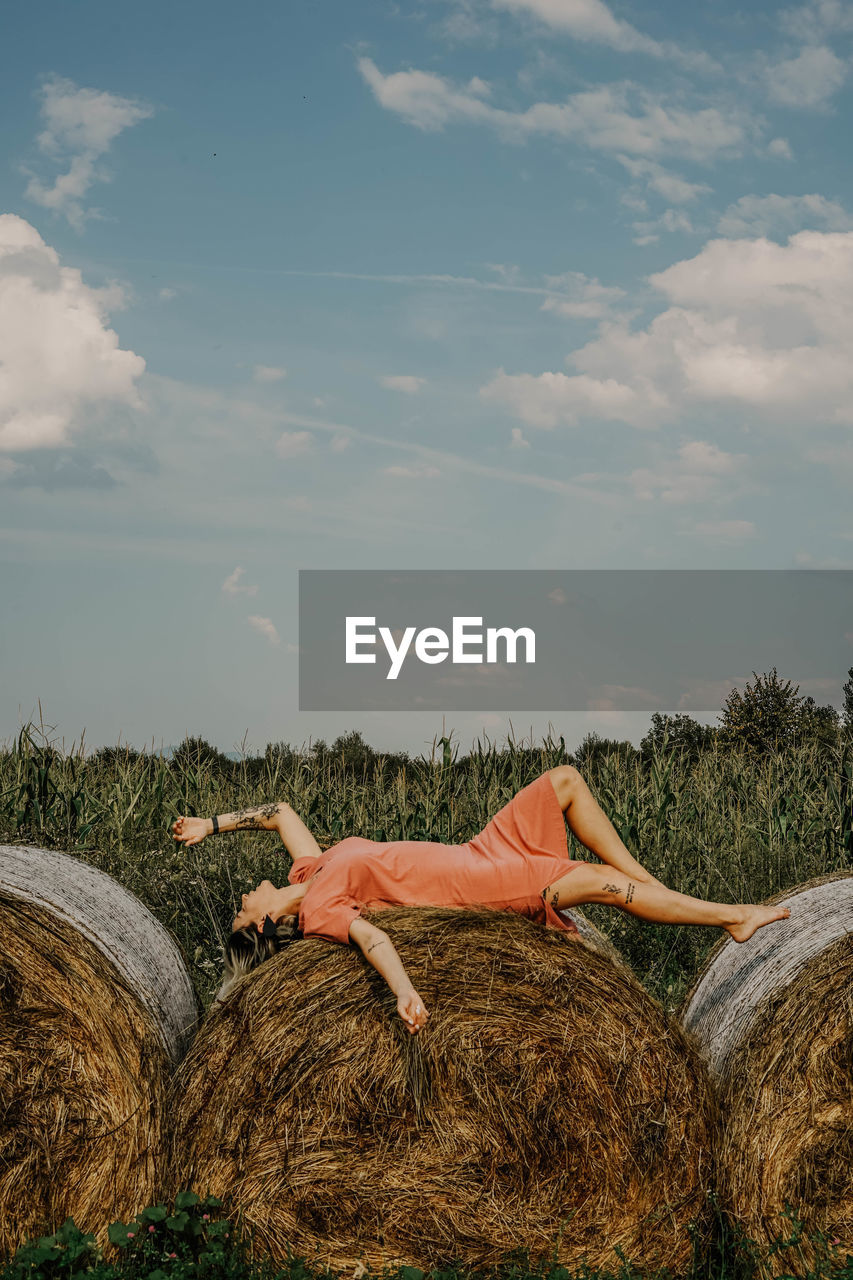 Full length of woman lying on hay bales against sky