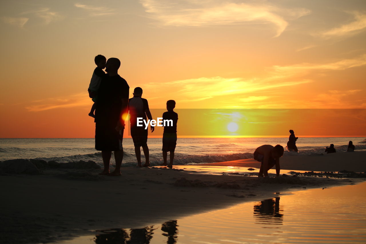 Silhouette people on beach against sky during sunset