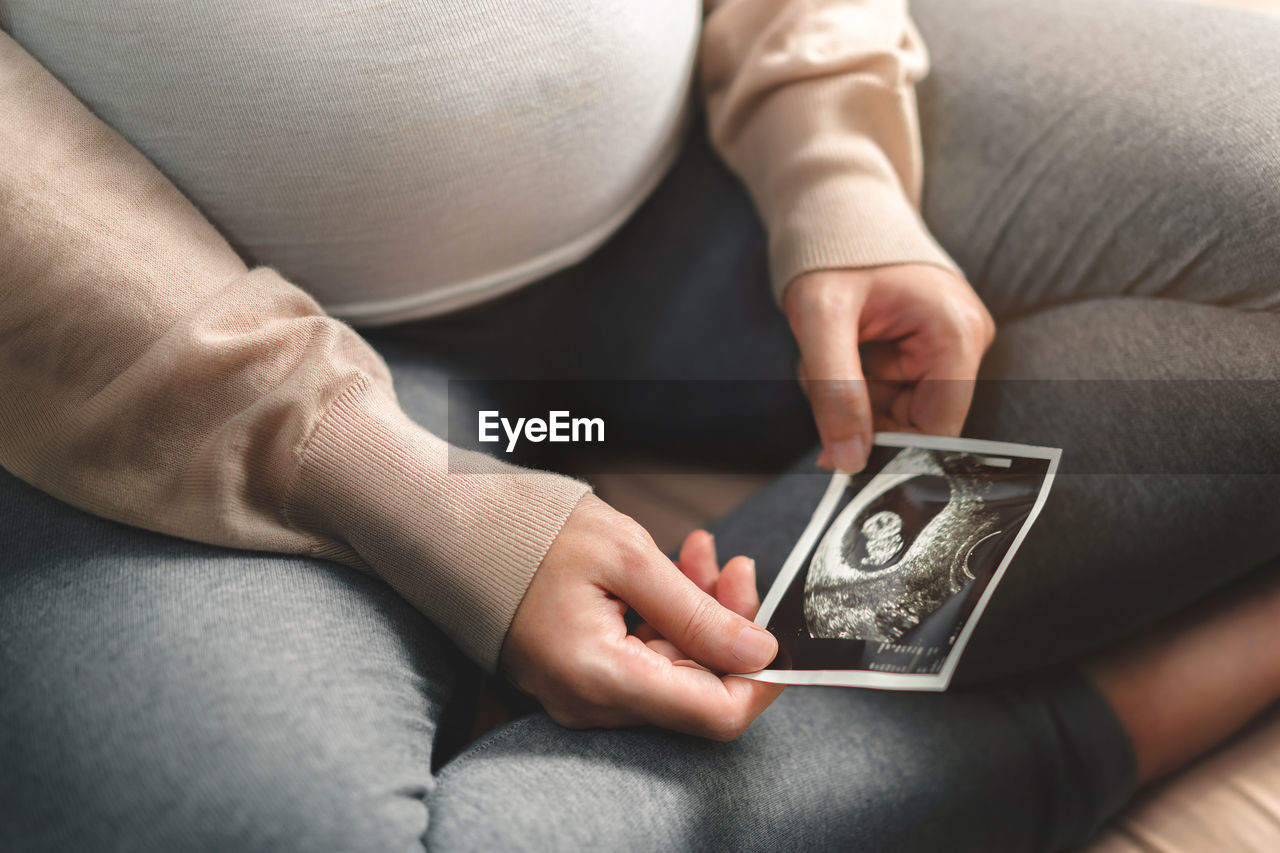 MIDSECTION OF WOMAN HOLDING WHILE SITTING ON FLOOR