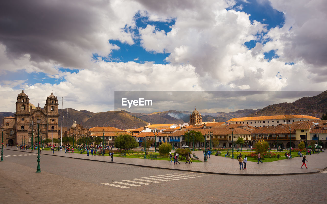 People walking on sidewalk in town against cloudy sky