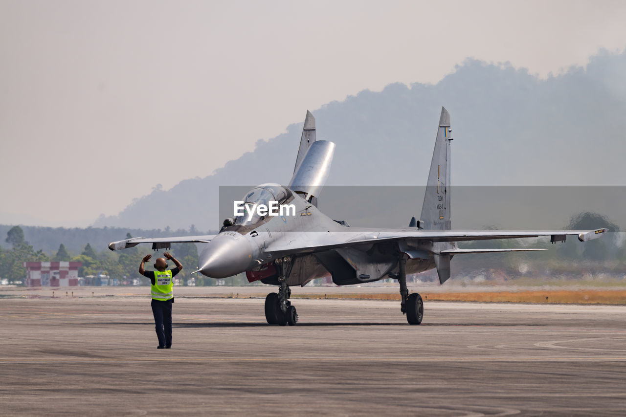 Man standing by air vehicle on runway against sky