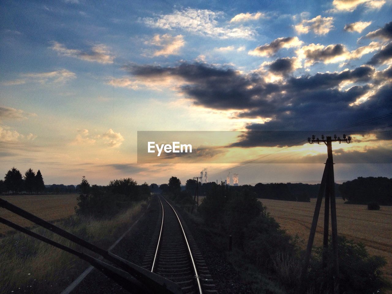 Railroad track amidst field seen through windshield of locomotive against cloudy sky