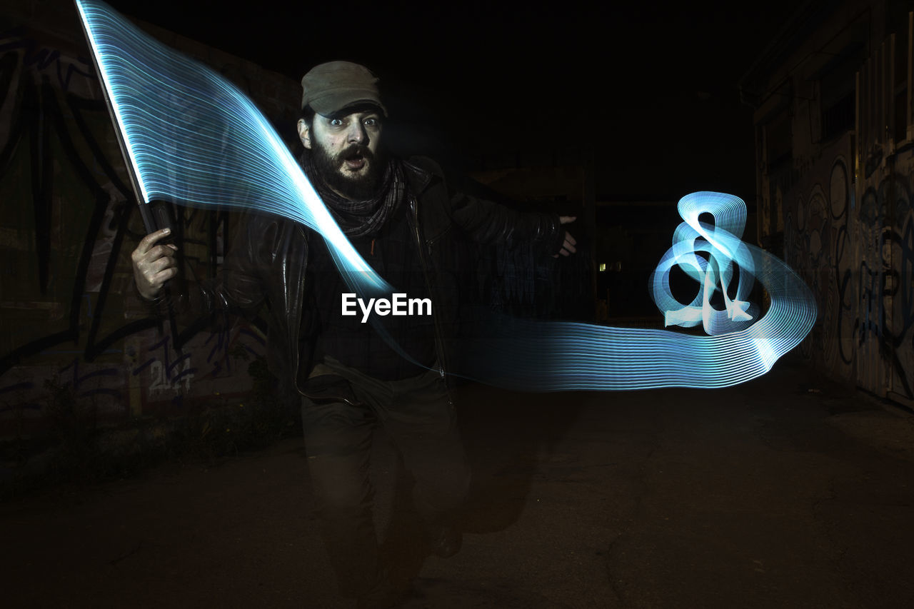 Digital composite image of mature man with light painting on street amidst graffiti wall