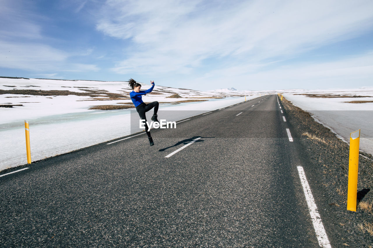 Woman jumping on road against sky during winter