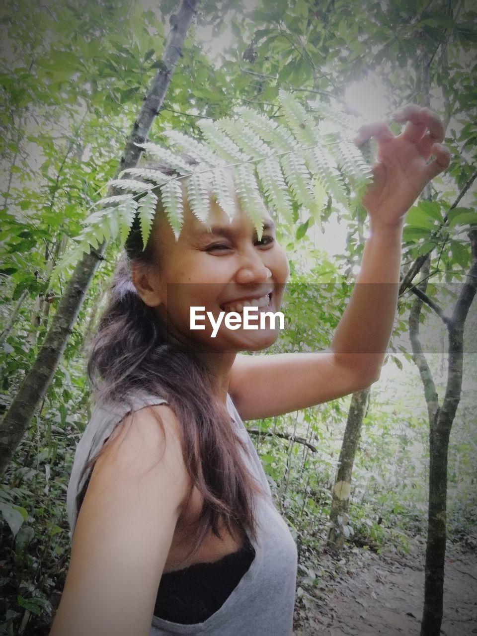 Portrait of smiling woman holding plant against trees