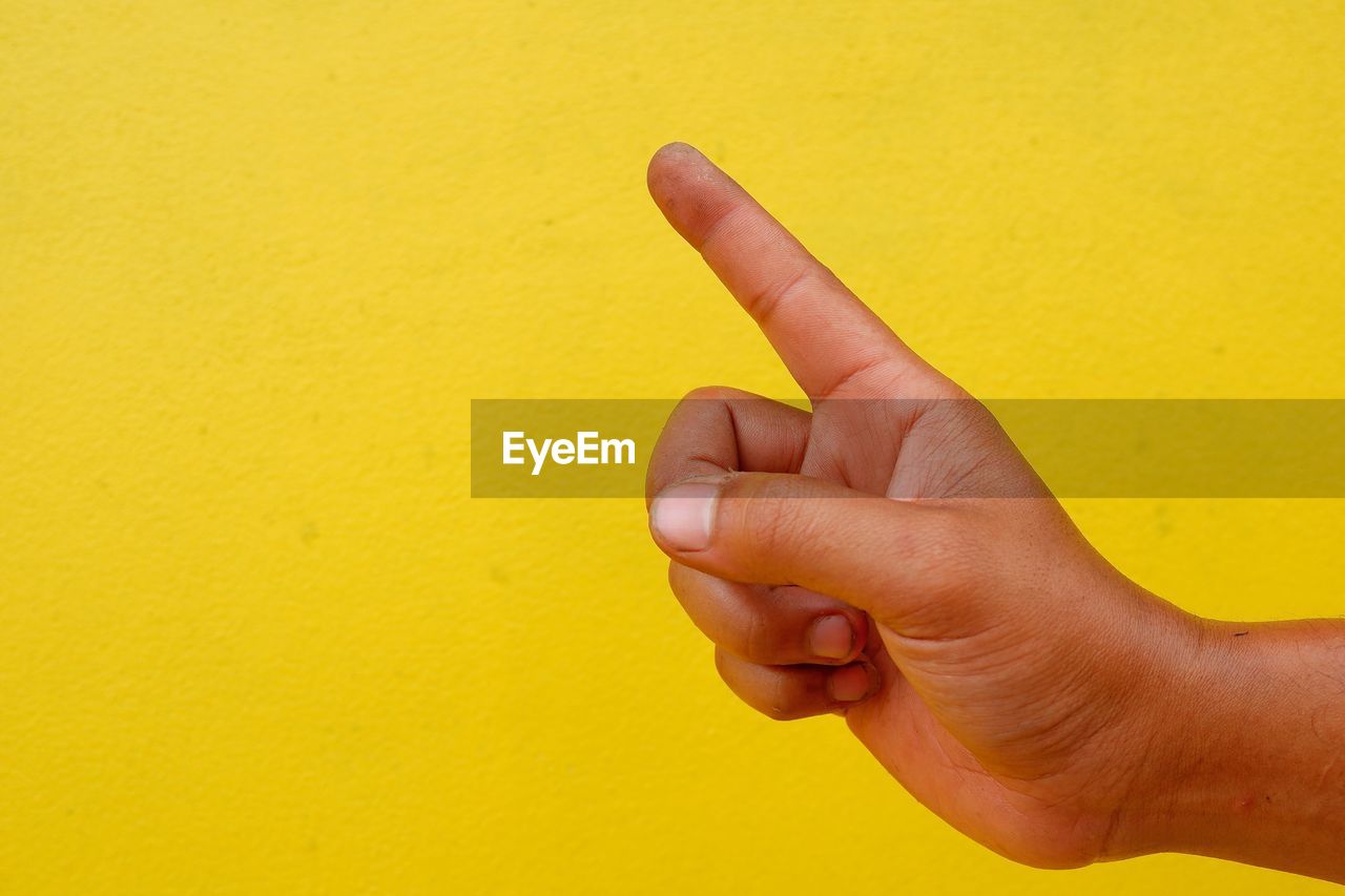 Cropped hand pointing against yellow wall