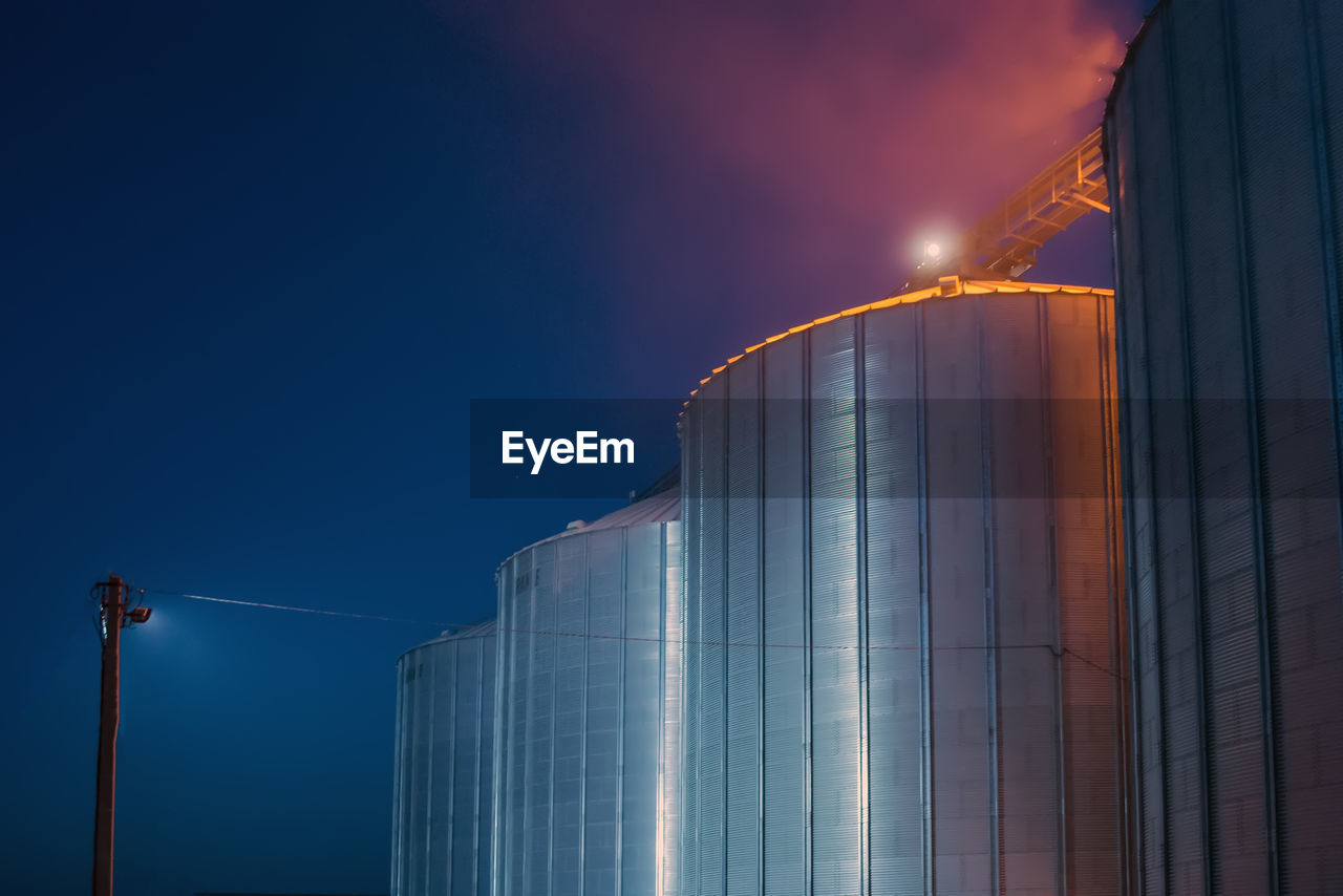 LOW ANGLE VIEW OF ILLUMINATED INDUSTRY AGAINST SKY AT DUSK