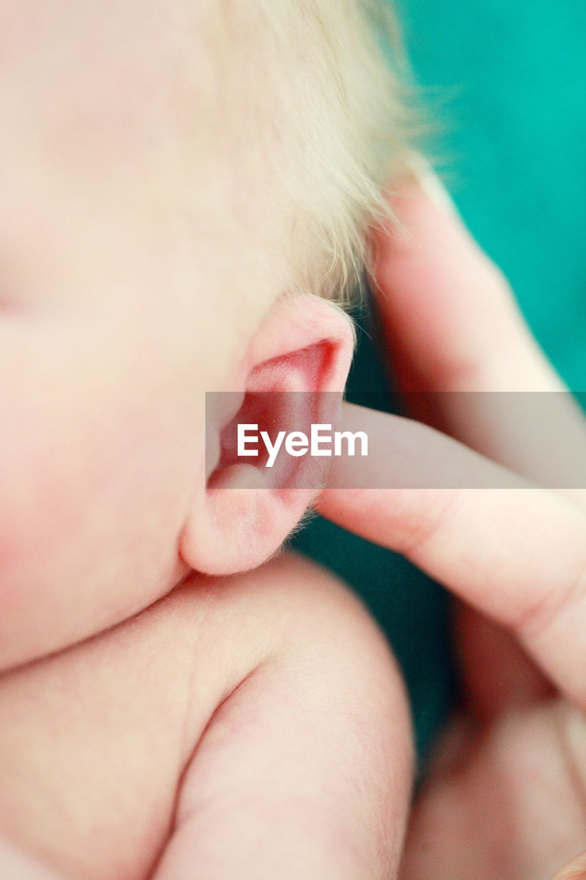 Cropped hand of person touching baby boy ear