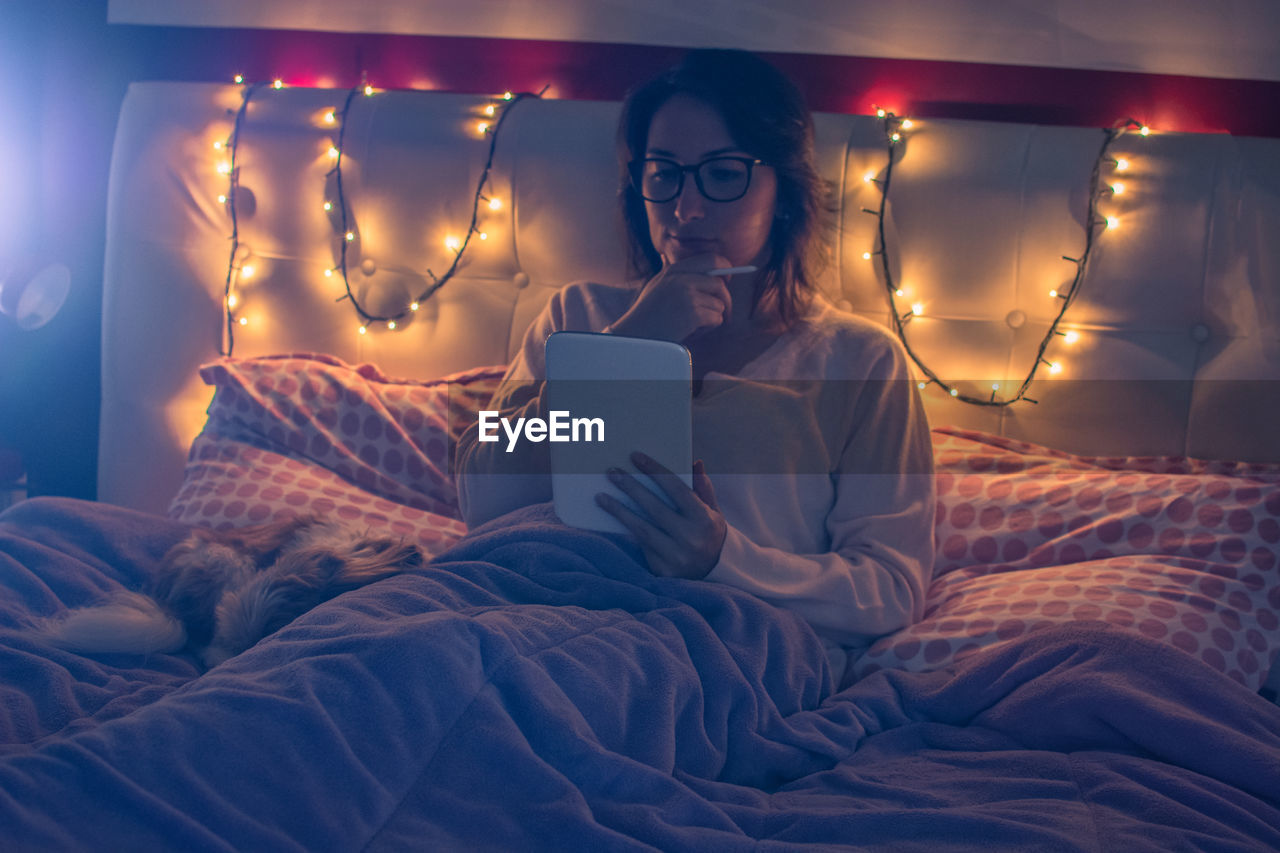 Young woman using digital tablet while sitting on bed at home