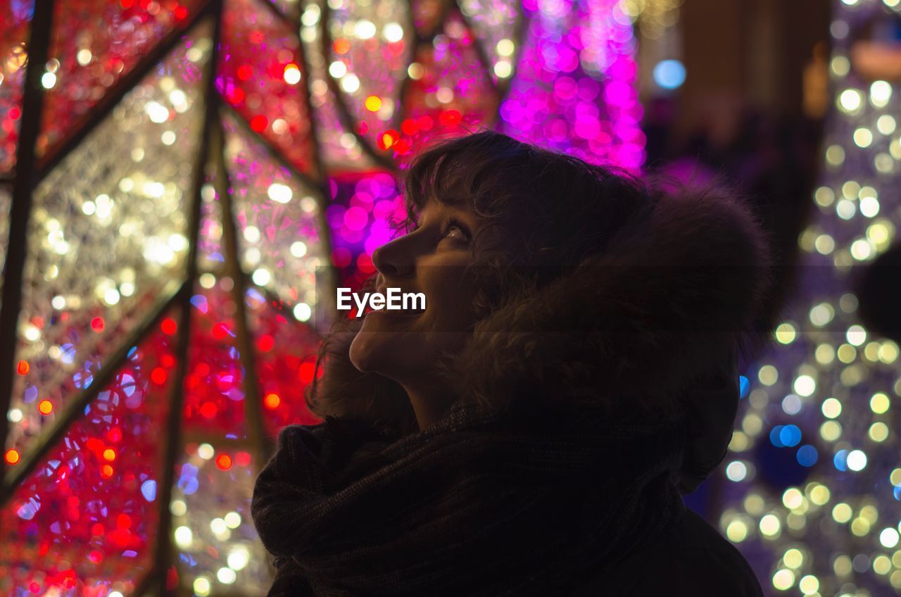 Happy beautiful woman wearing fur clothing against illuminated decoration