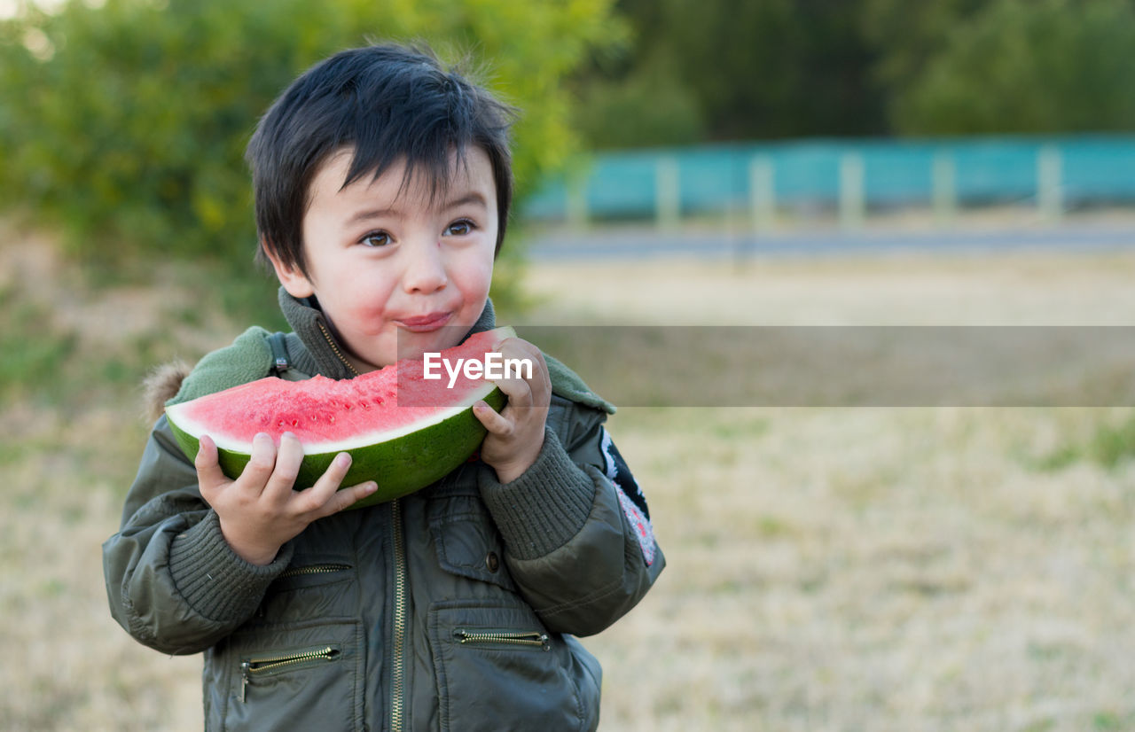 Boy eating watermelon while standing at park
