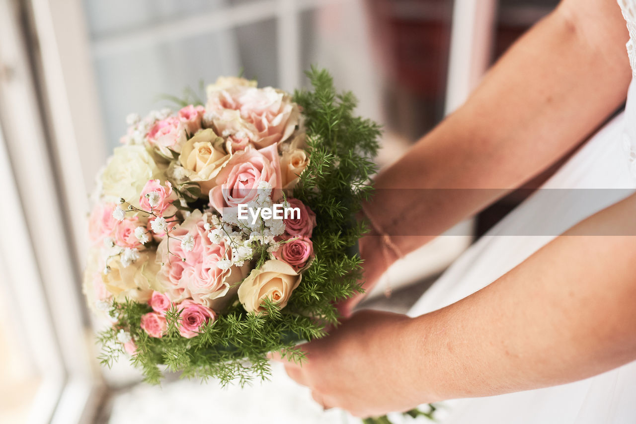 Midsection of bride holding rose bouquet