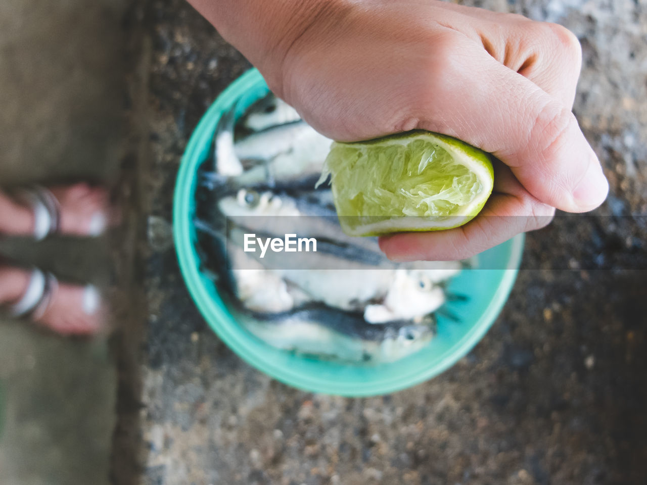 Cropped image of hand squeezing lemon on fish in container
