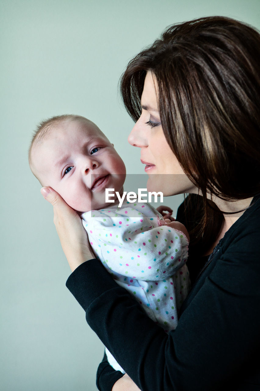 Mother carrying cute daughter while standing against wall