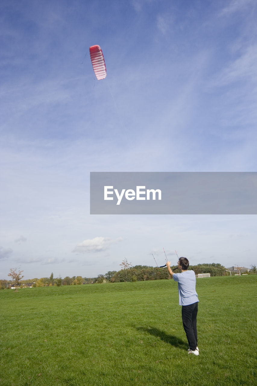 Man with paragliding on grassy field against sky during sunny day