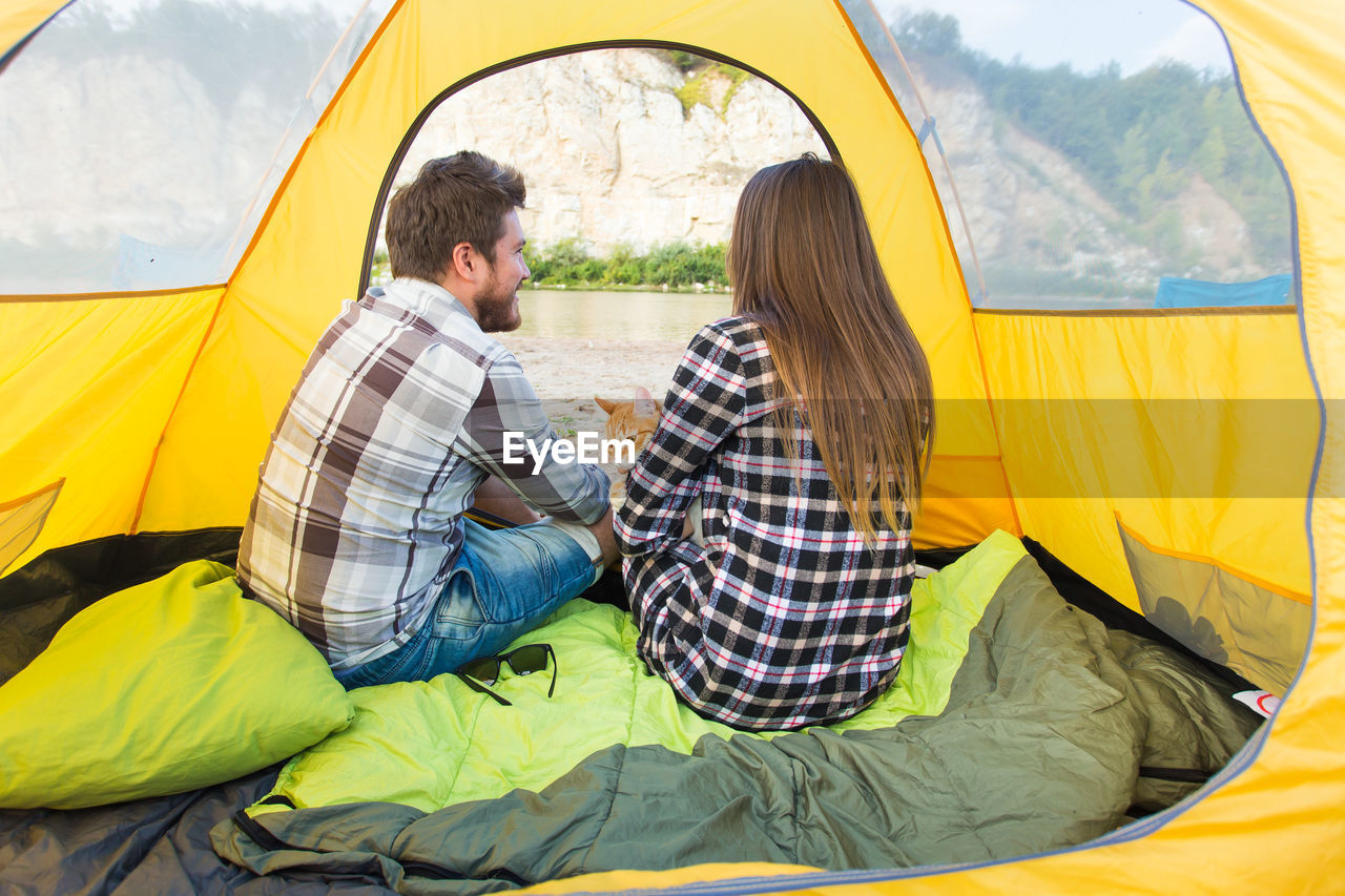 REAR VIEW OF COUPLE SITTING ON TENT