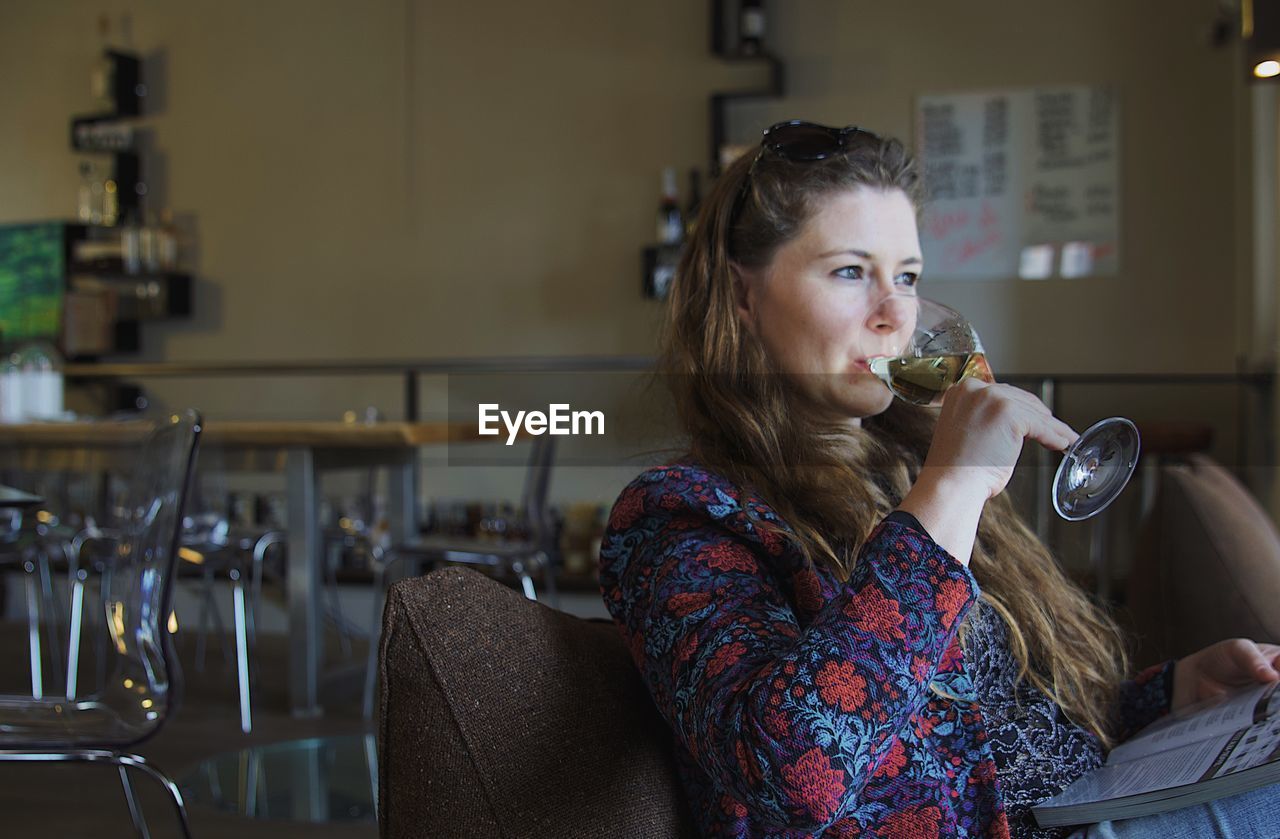 Woman drinking wine while sitting with book at restaurant table