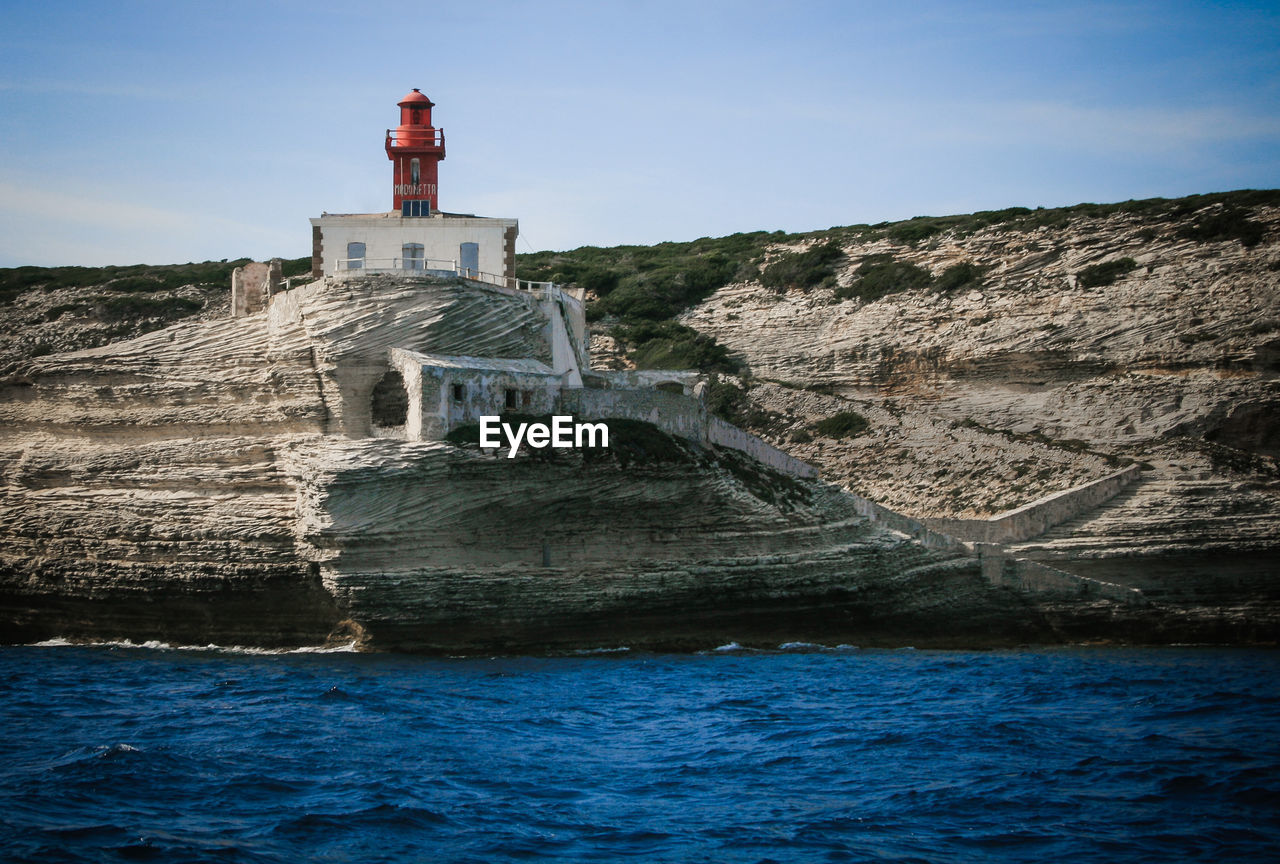 Lighthouse on cliff by sea against clear blue sky