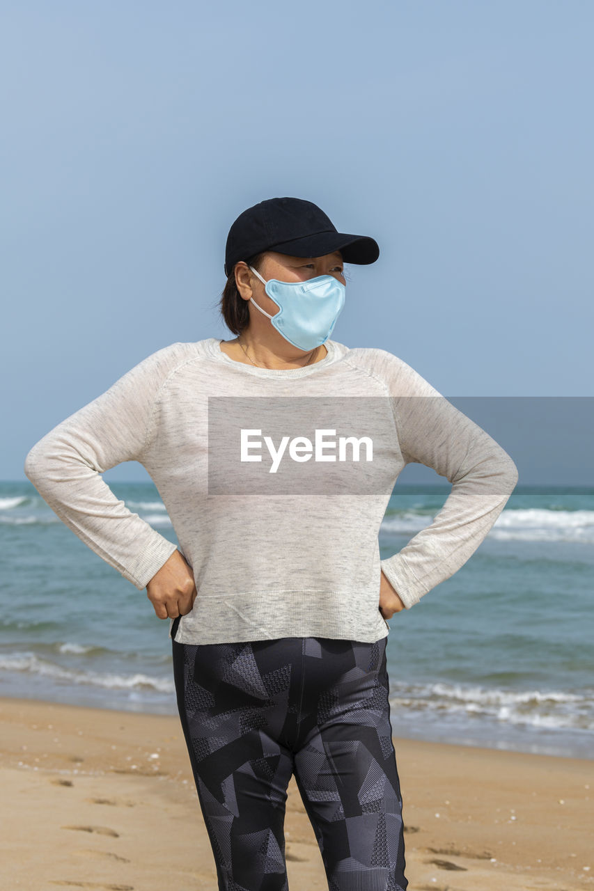 Woman wearing mask standing against sea and sky