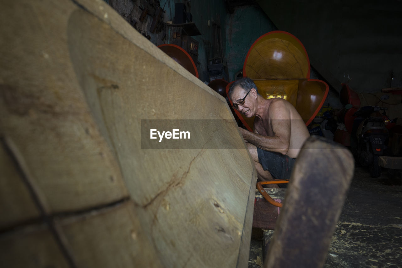 Side view of shirtless senior carpenter working in workshop