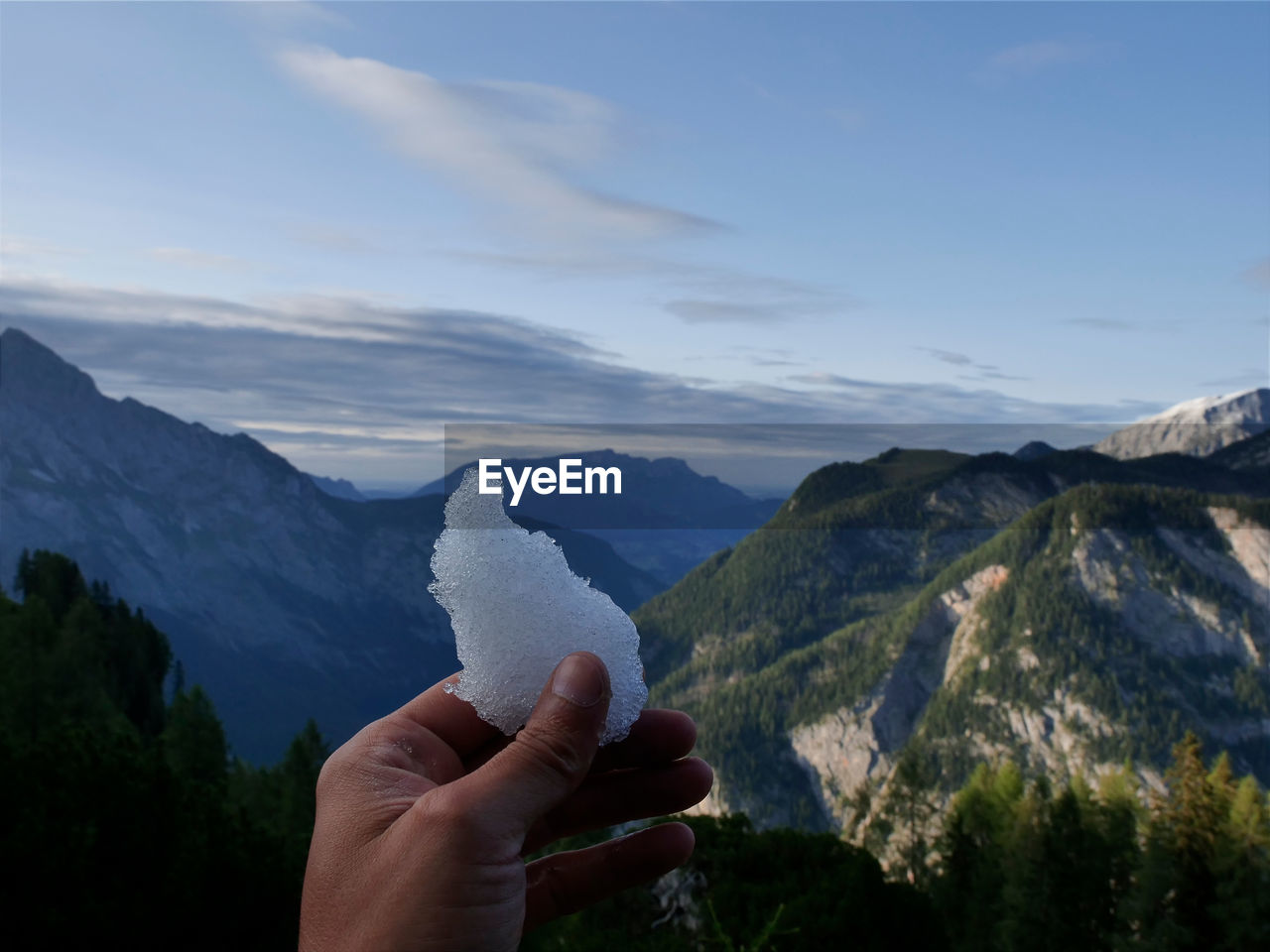 Cropped hand holding ice against mountain range