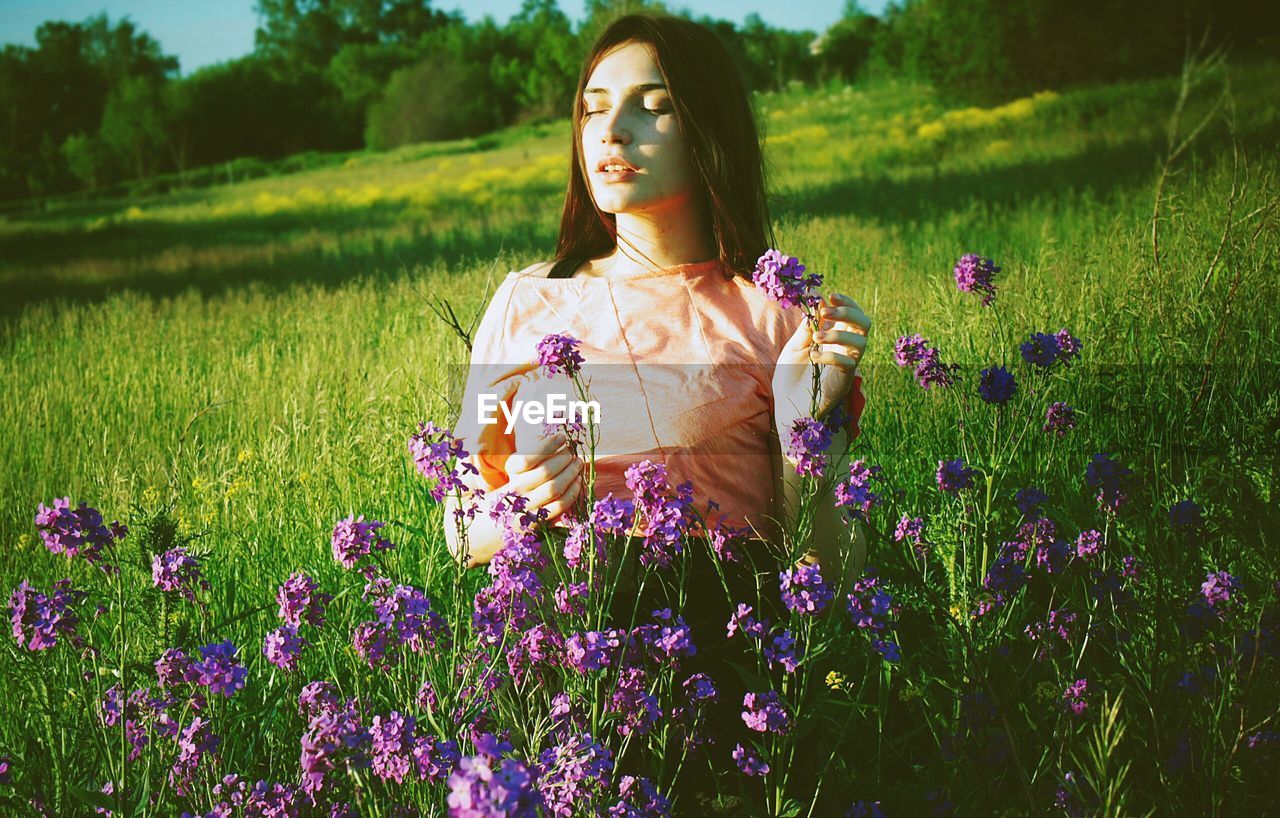Young woman touching purple flowers on grassy field