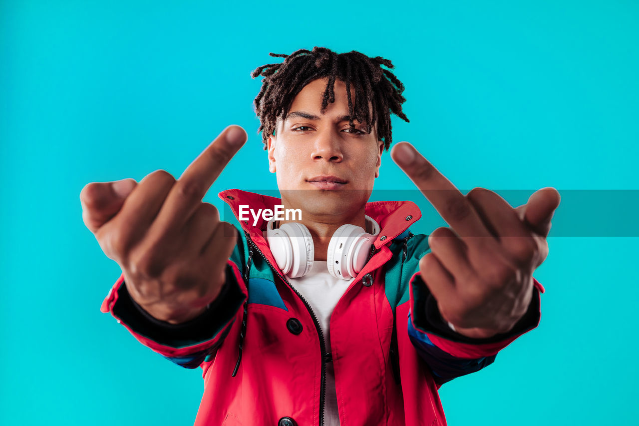 one person, colored background, portrait, studio shot, gesturing, sports, young adult, blue, adult, men, emotion, looking at camera, waist up, front view, arm, person, indoors, clothing, athlete, success, sports clothing, hand, blue background, human limb, limb, facial expression, standing, anger, arms raised, serious, sign language, hand sign