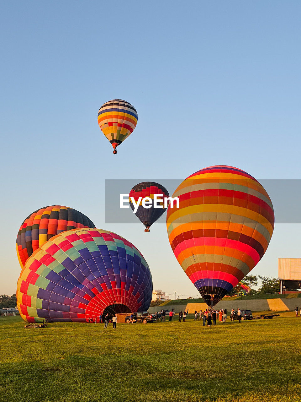hot air balloon, hot air ballooning, balloon, air vehicle, vehicle, aircraft, transportation, multi colored, mid-air, flying, adventure, mode of transportation, ballooning festival, basket, toy, sky, nature, travel, taking off, environment, journey, recreation, blue, container, heat, leisure activity, celebration, flame, traditional festival, clear sky, burning, morning, tradition, executive car, cloud, travel destinations, sports, tourism, outdoors, motion, fire, landscape, grass, day, holiday, fun, trip, outdoor pursuit, group of objects, vacation, no people, field