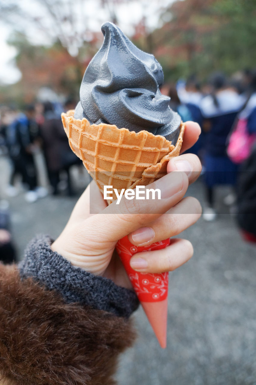 CLOSE-UP OF HAND HOLDING ICE CREAM CONE OUTDOORS