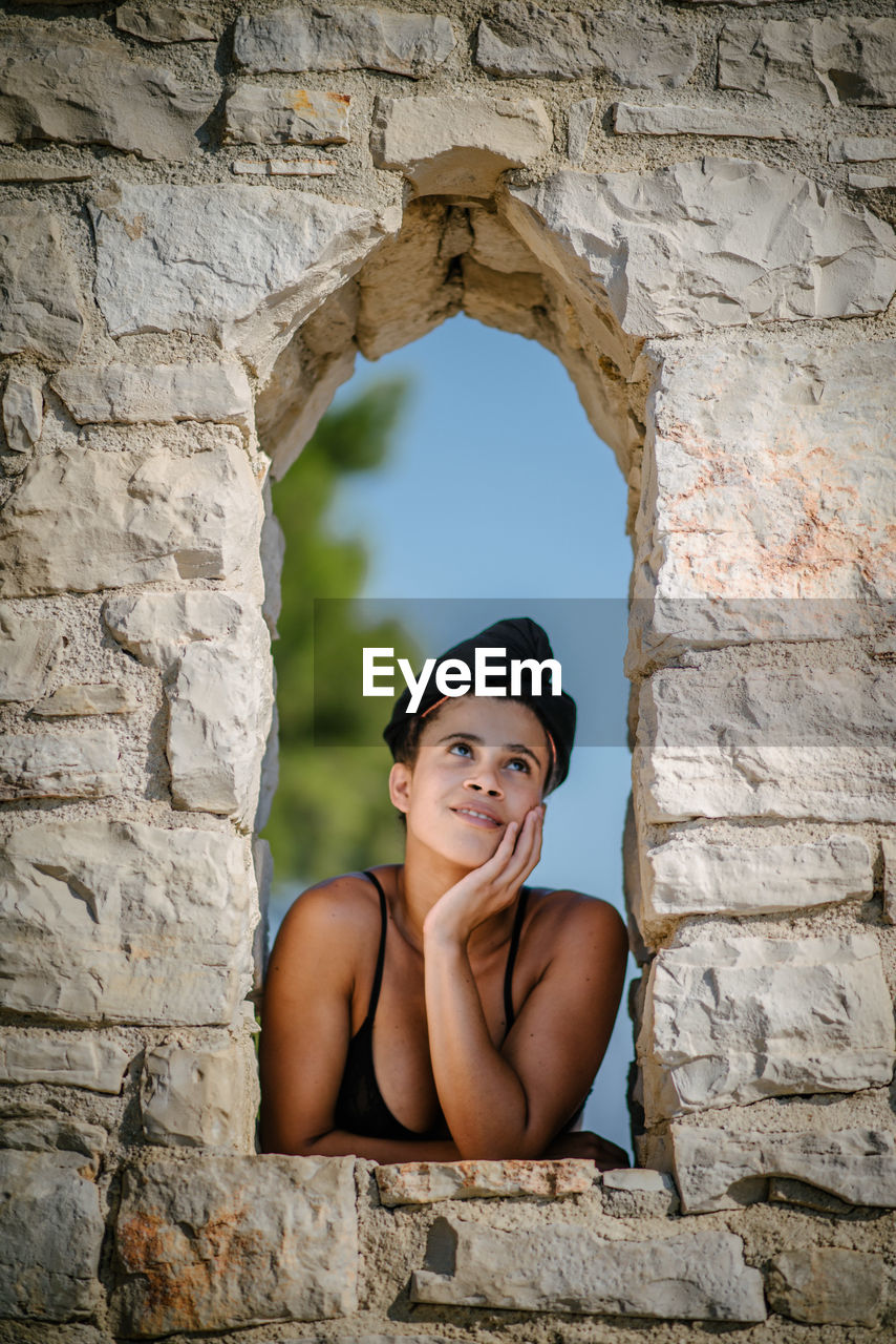 Thoughtful woman leaning on stone wall window