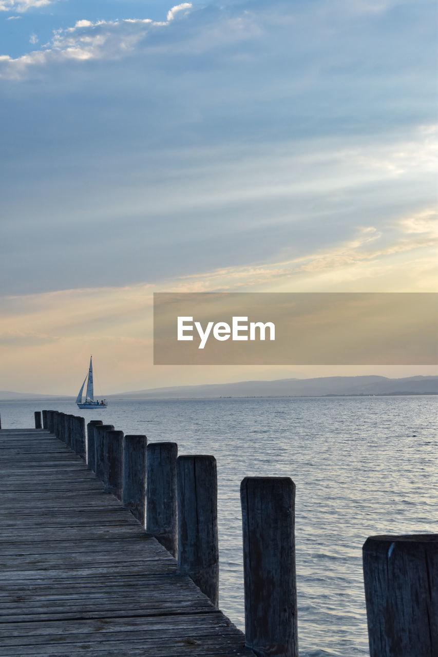 Wooden pier in sea against sky during sunset