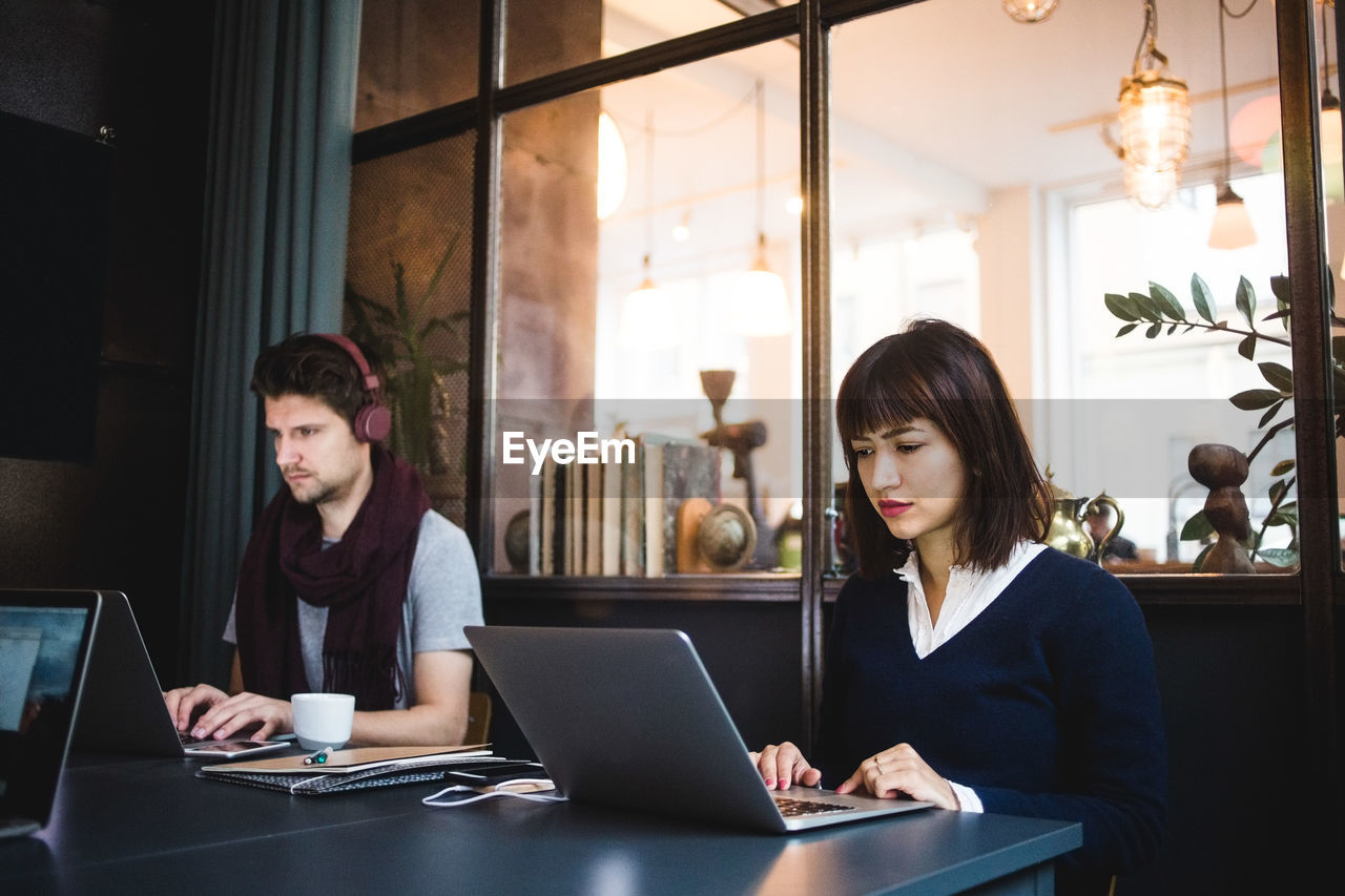 Confident female and male entrepreneurs using laptops at desk in office