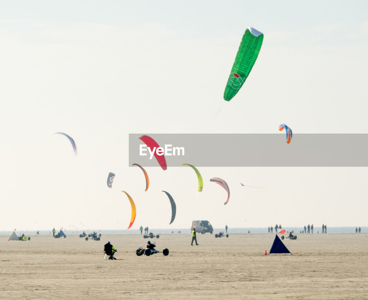 Multi colored parachutes fling over beach against clear sky