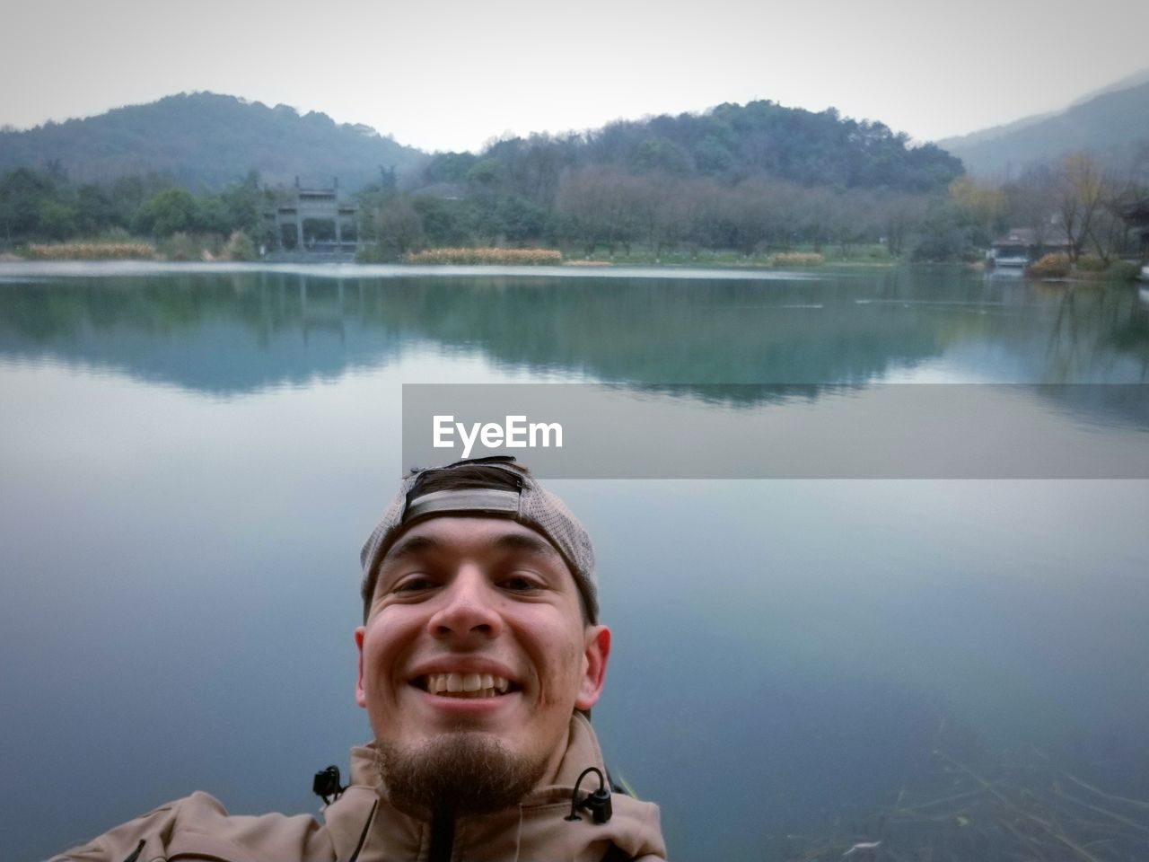 Portrait of smiling young man by lake against mountains