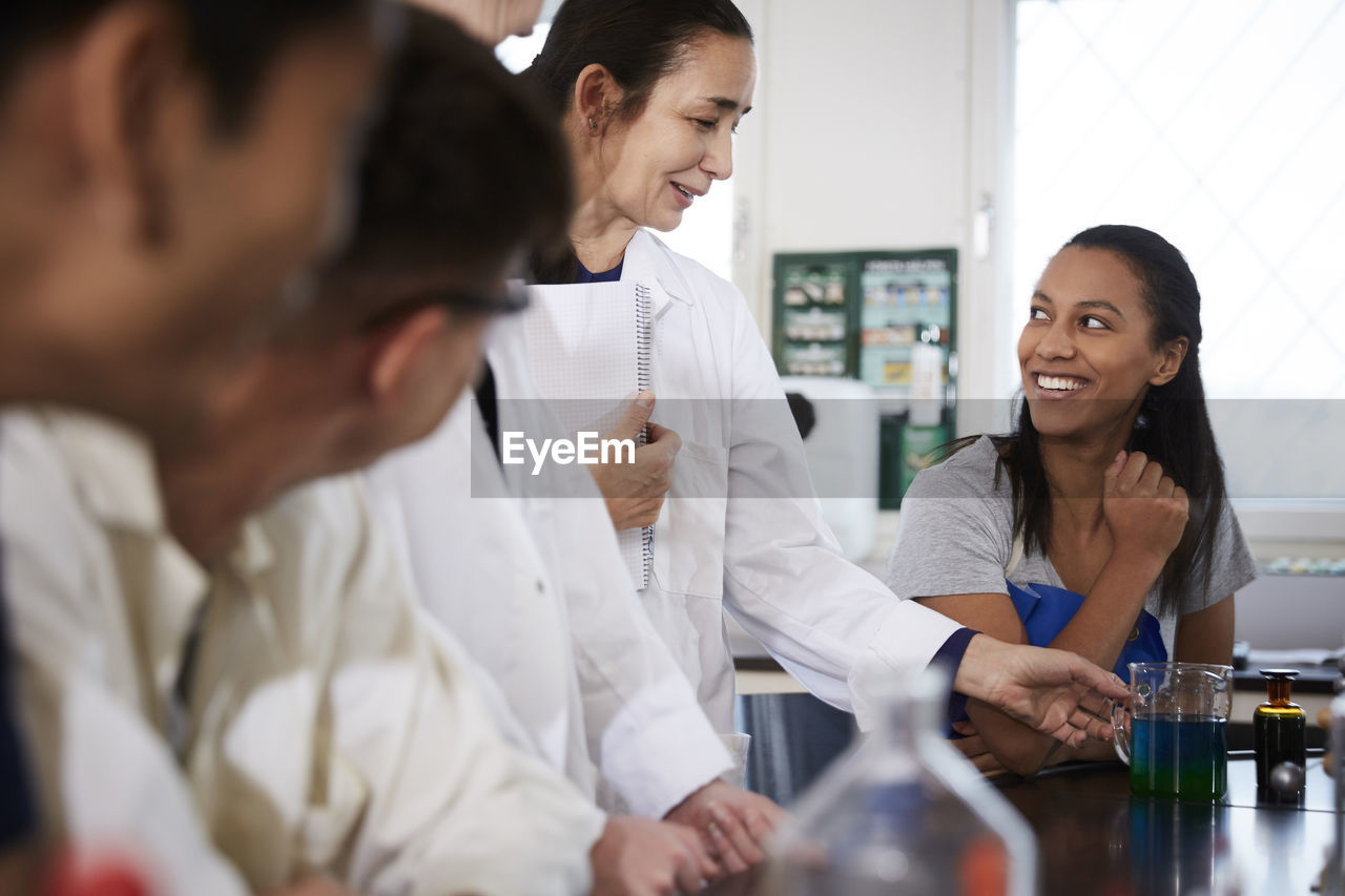 Mature teacher looking at solution in beaker amidst young multi-ethnic students