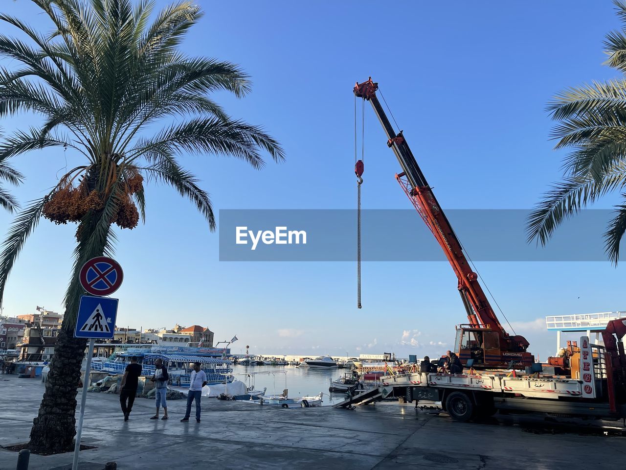 palm tree, tropical climate, tree, sky, nature, walkway, water, architecture, beach, sea, vacation, city, boardwalk, transportation, vehicle, coast, clear sky, plant, travel destinations, crane - construction machinery, business, outdoors, blue, day, machinery, built structure, mode of transportation, date palm, industry, travel