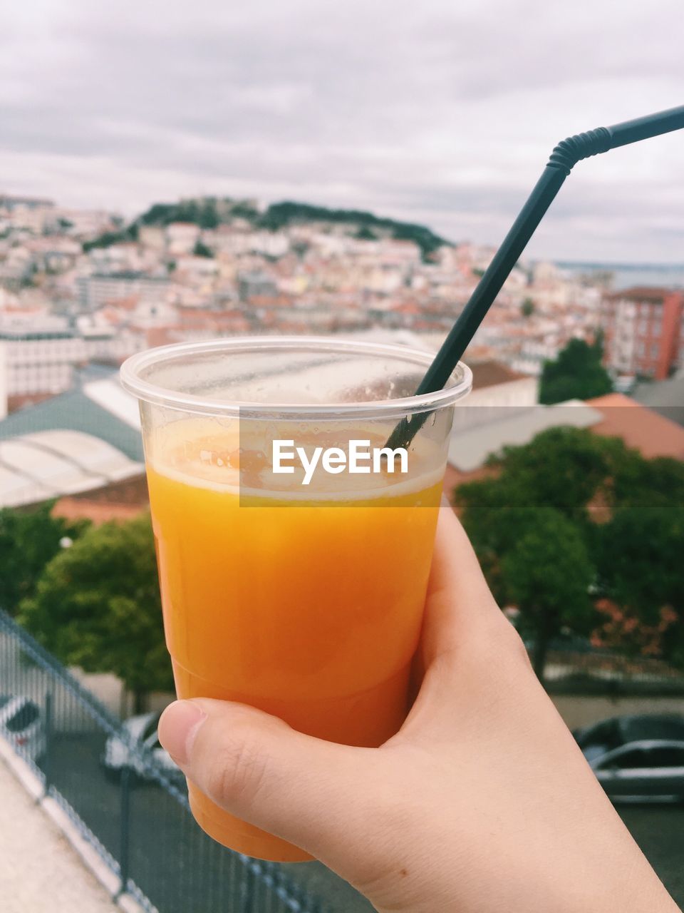 Cropped image of hand holding juice glass against cityscape