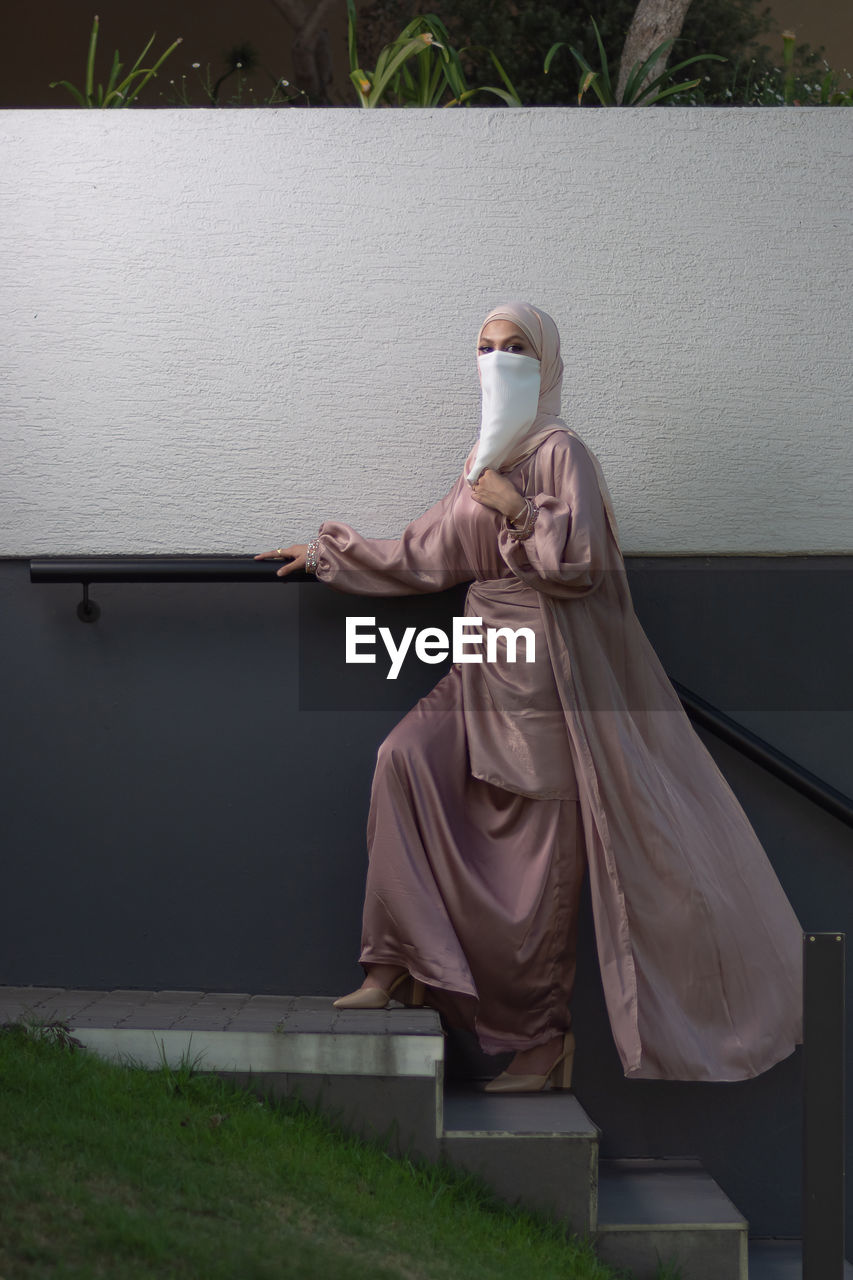 Full length view of veiled woman with white niqab and pink silky dress walking up the stairs