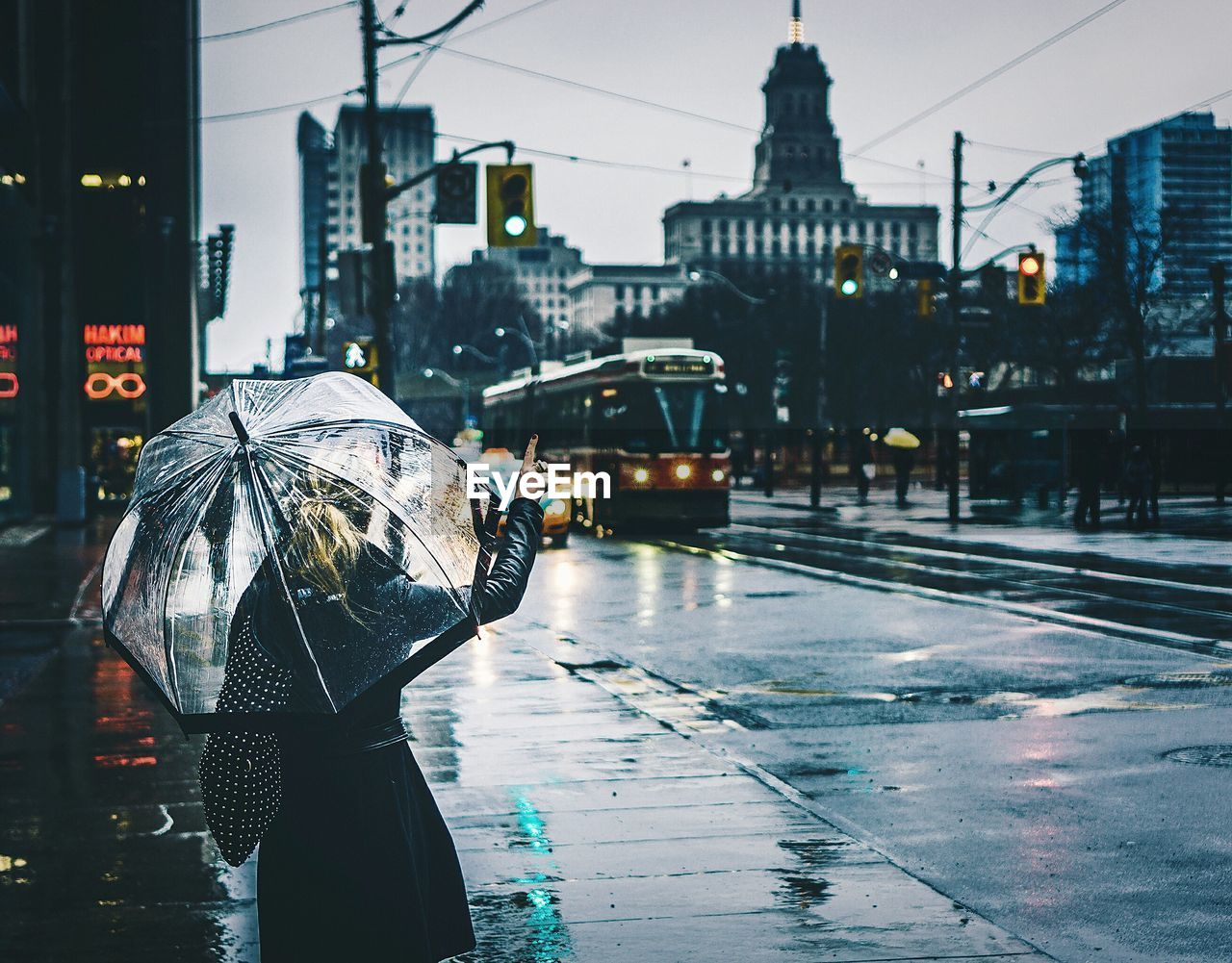 Rear view of woman with umbrella standing on wet city street during monsoon