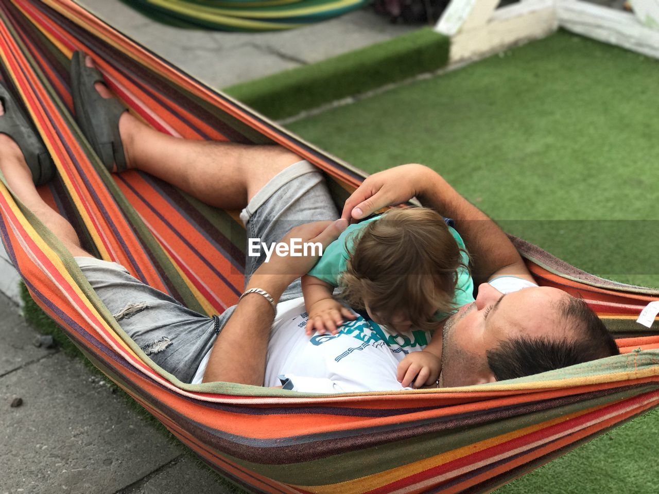 High angle view of father embracing baby while lying in hammock